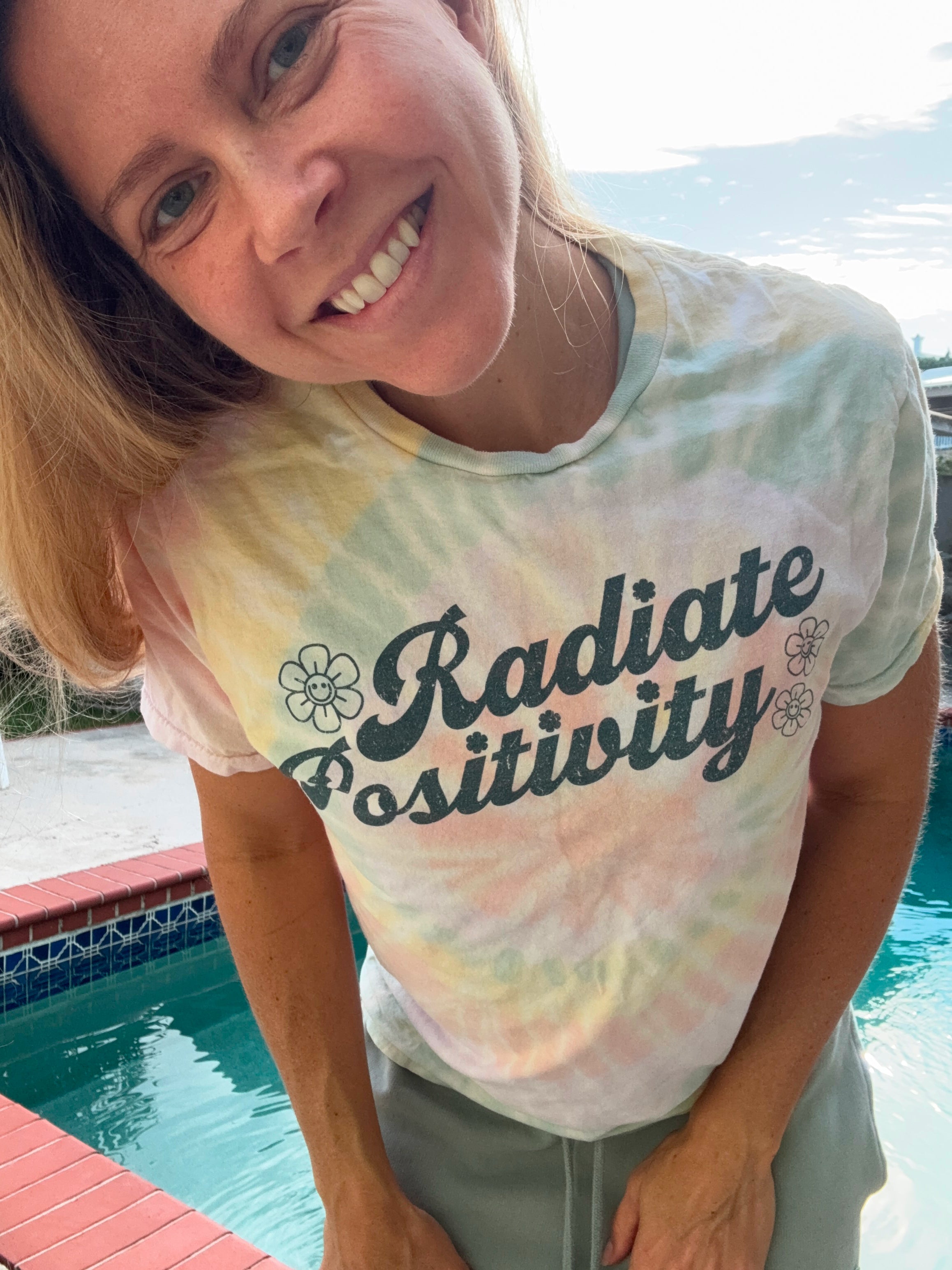 Amy wearing a tie dye Radiate Positivity t-shirt by the pool